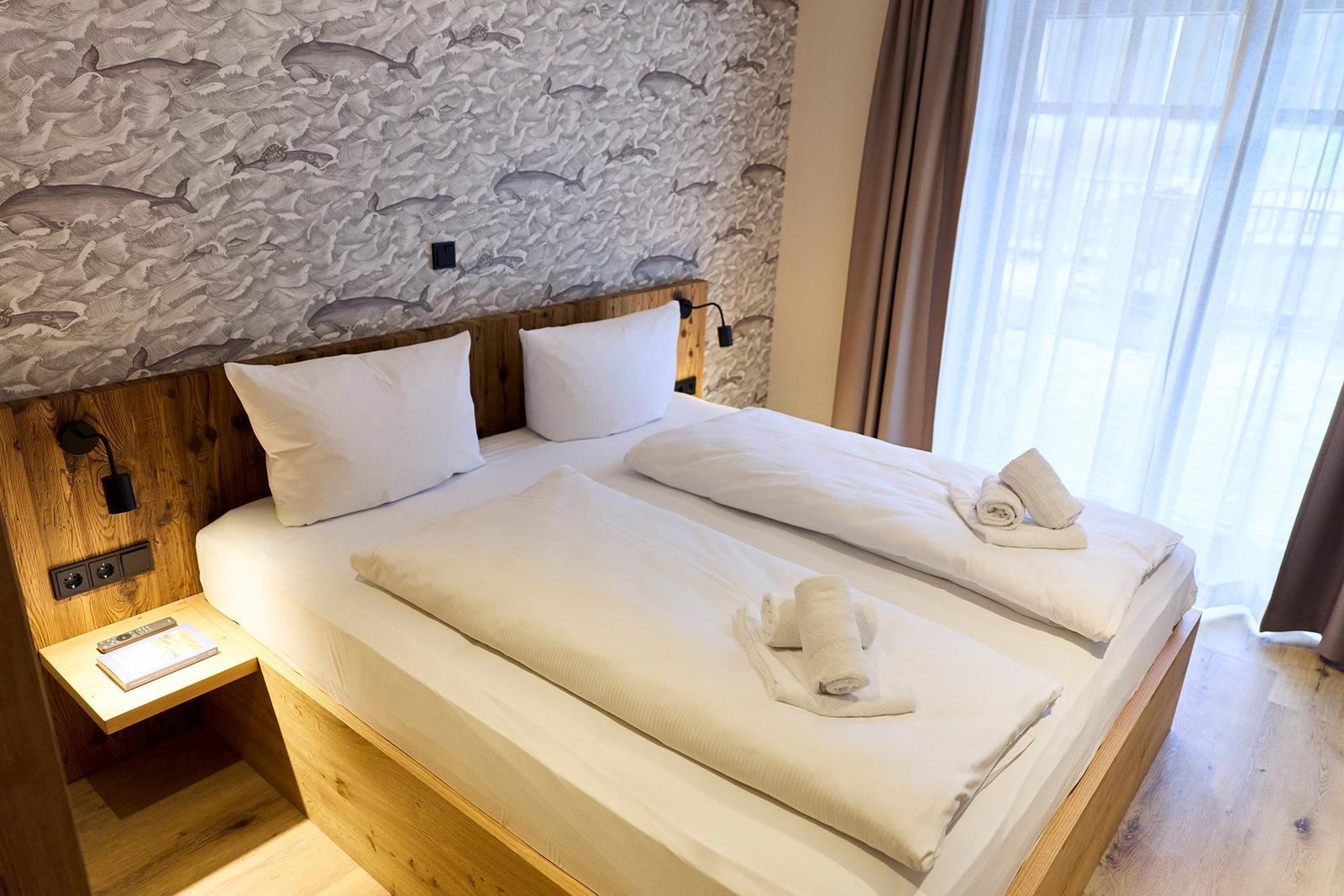 Doppelbett mit weißen Bettwäsche und Falttüchern. Wand mit Fischmotiv und Holzgestell.