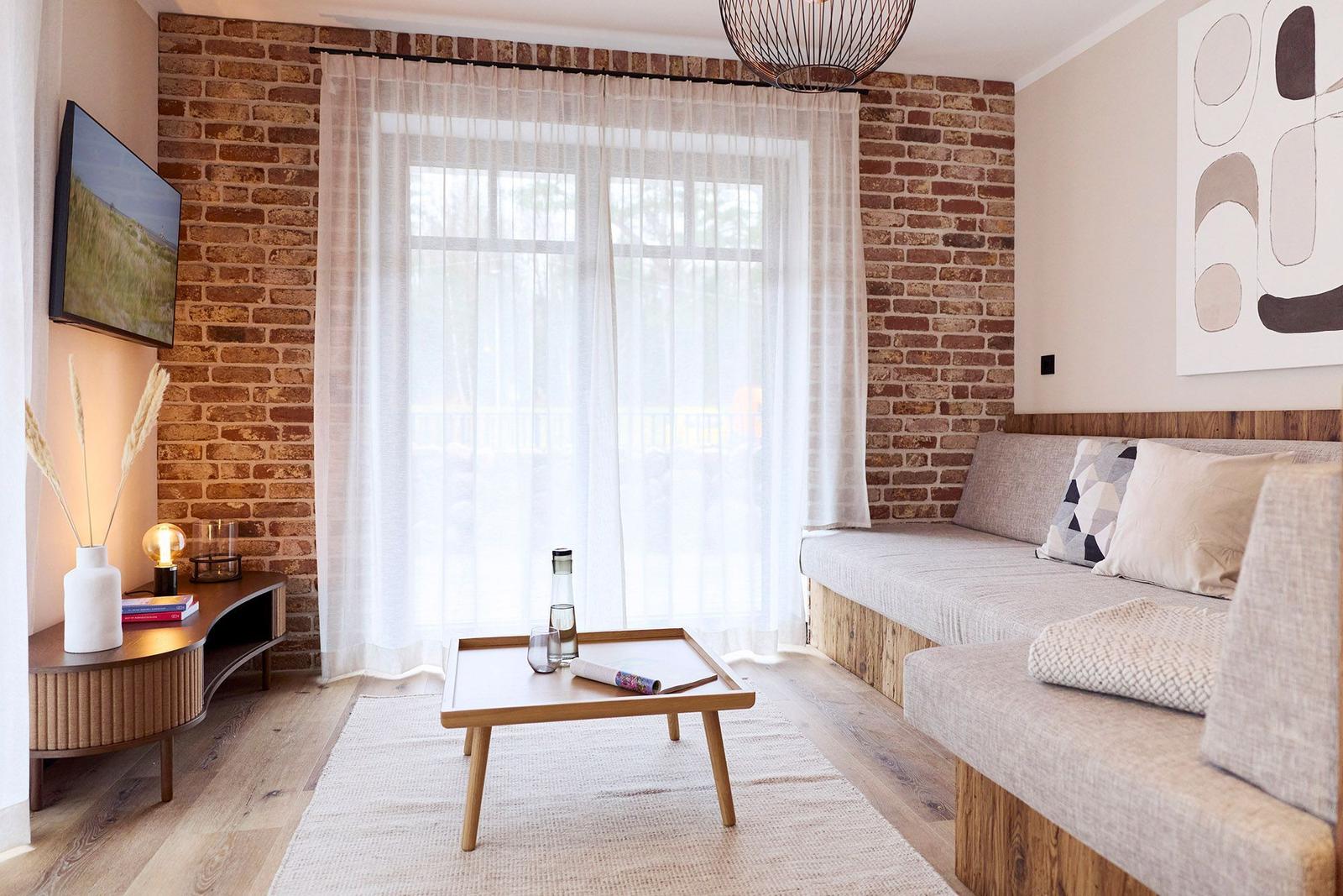 Wohnzimmer mit Sofa, Couchtisch und Fernseher an Backsteinwand.
