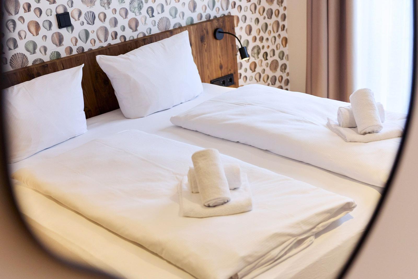 Ein Bett mit weißen Bettwäsche und Handtüchern. Wand mit Muschel-Motiv und Holzkopfteil.
