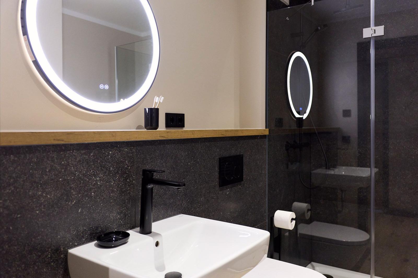 Badezimmer mit Waschbecken, beleuchtetem Spiegel und Dusche