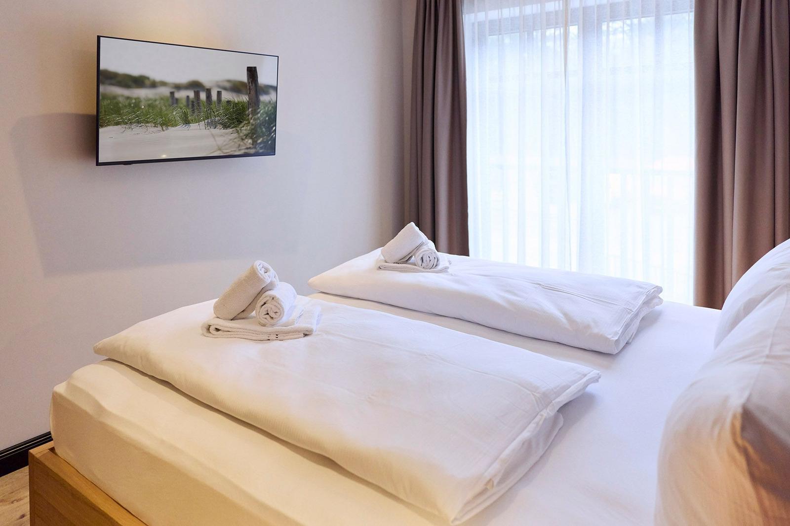 Schlafzimmer mit Bett, weißen Bettwäsche und TV an der Wand.