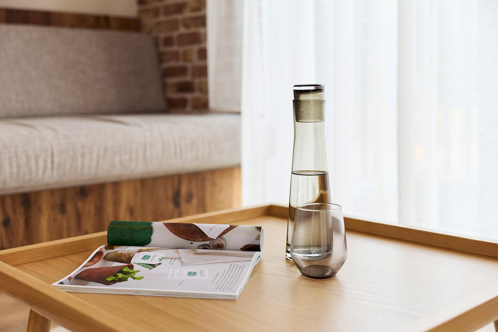 Auf dem Tisch steht eine Wasserflasche und ein Glas. Im Hintergrund ist ein Sofa zu sehen.