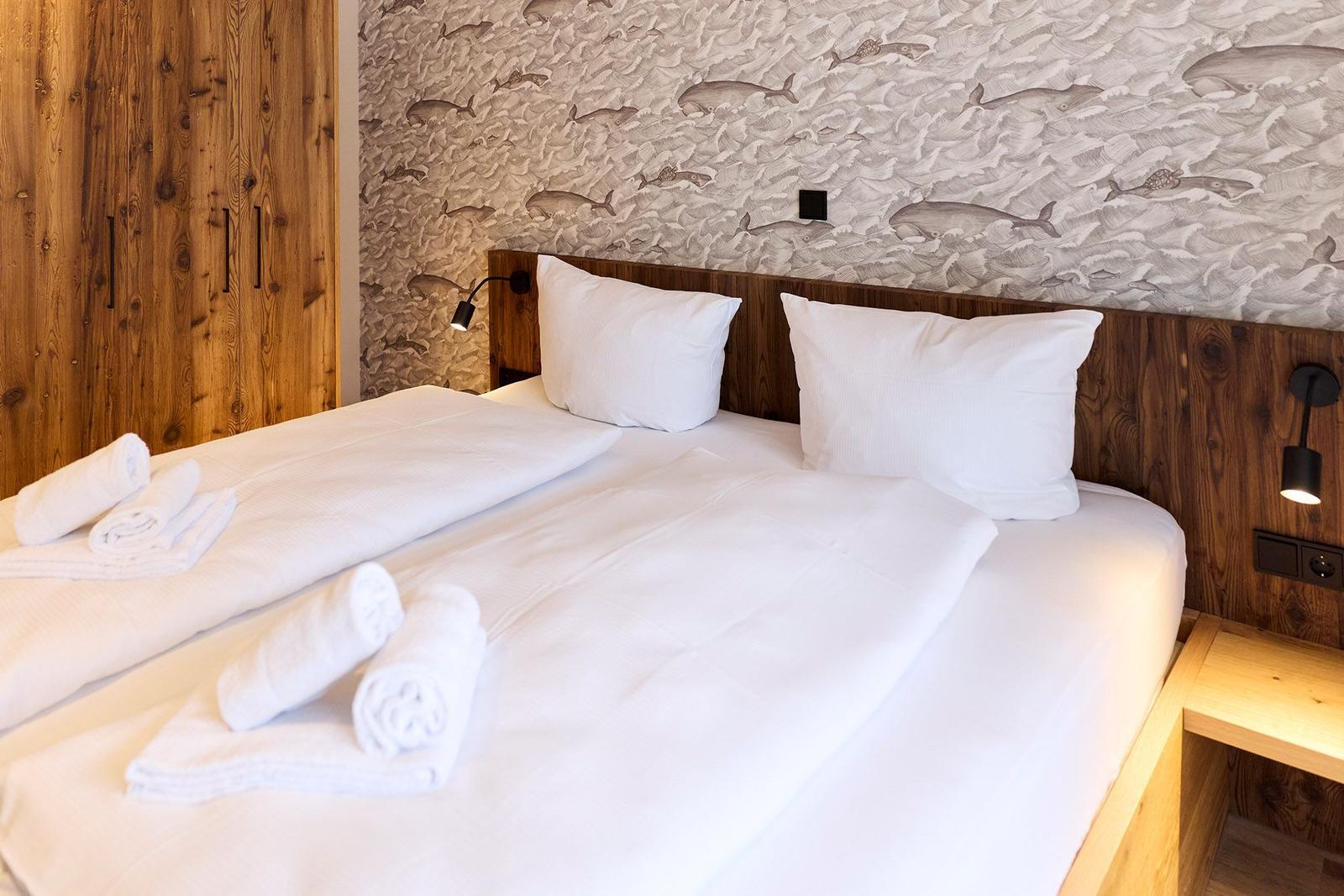 Schlafzimmer mit Bett, weißen Kissen und Handtüchern. Wandtapete mit Fischmotiven und Holzelemente.