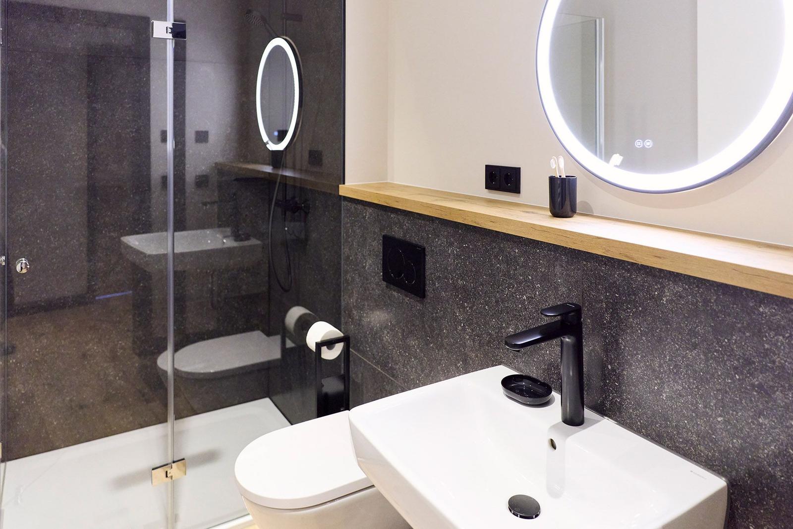 Badezimmer mit Dusche, Waschbecken und beleuchtetem Spiegel