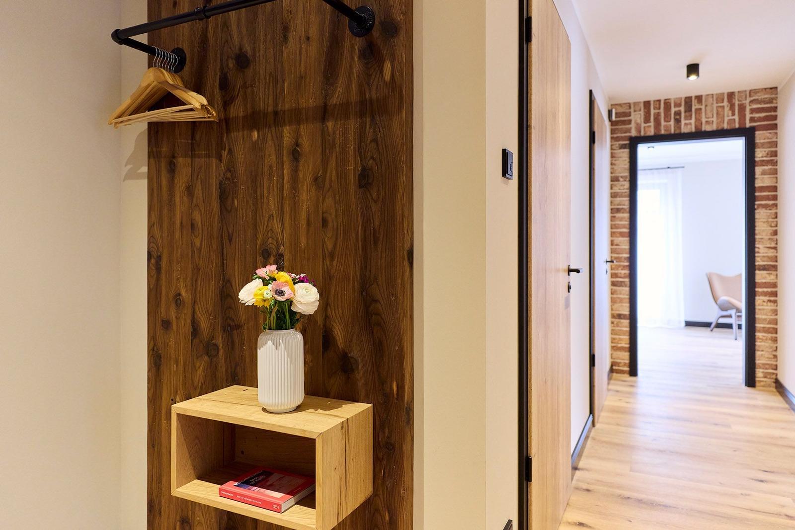 Holzwand mit Haken, Blumen und Regal im Flur. Tür führt in Wohnbereich mit Steinwand.