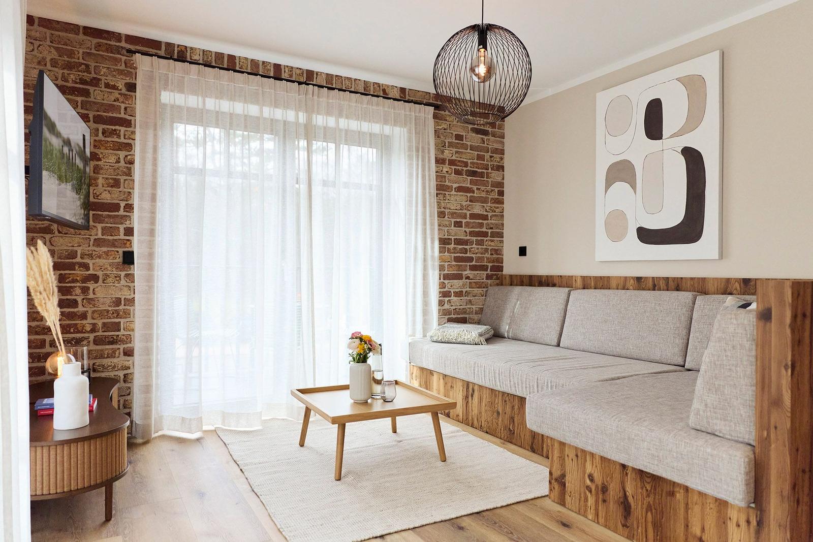 Wohnzimmer mit Sofa, Tisch und Fenster. Wand aus Backstein, Wandbild und Hängelampe.