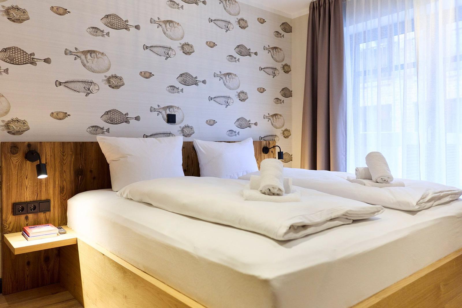 Schlafzimmer mit Bett, Fischmotiv-Wand und Fenster mit Vorhängen.