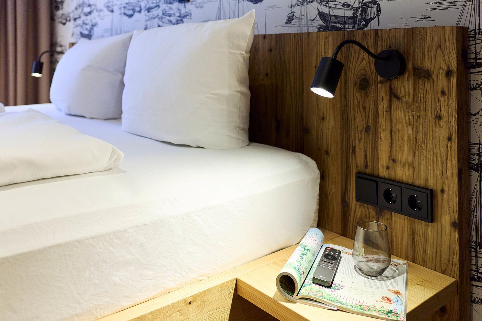 Schlafzimmer mit Bett, Holz-Kopfteil und Nachttisch mit Glas und Fernbedienung.