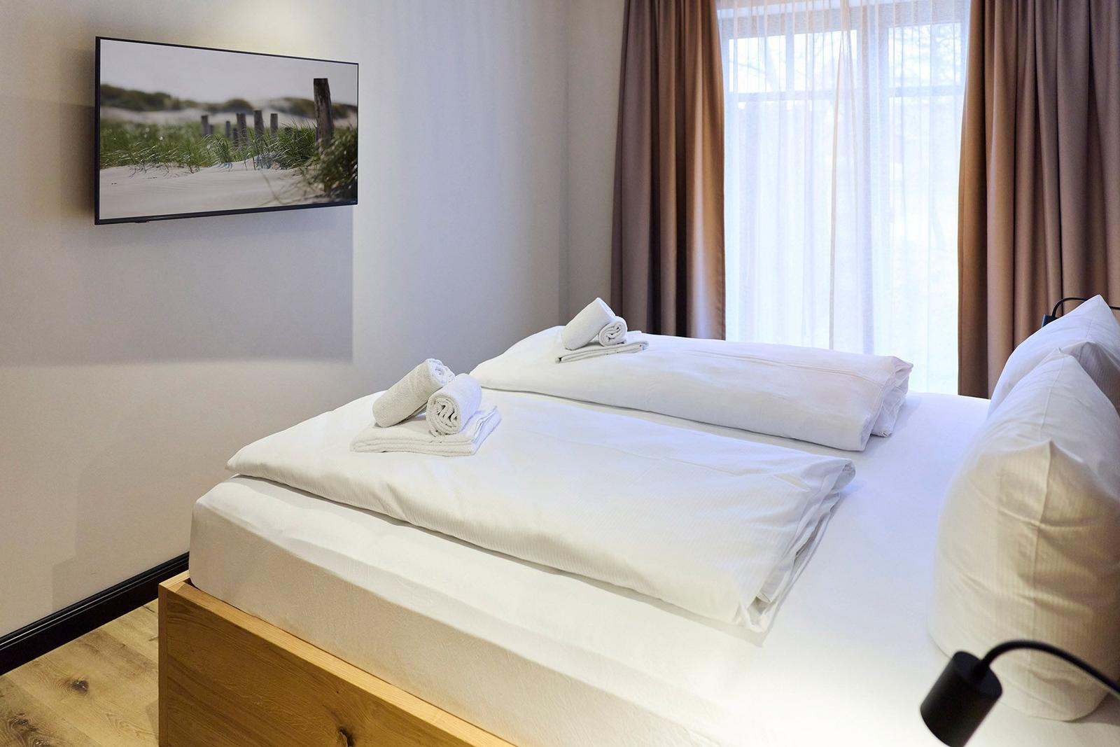 Schlafzimmer mit Doppelbett, weißen Bettwäsche und TV an der Wand.