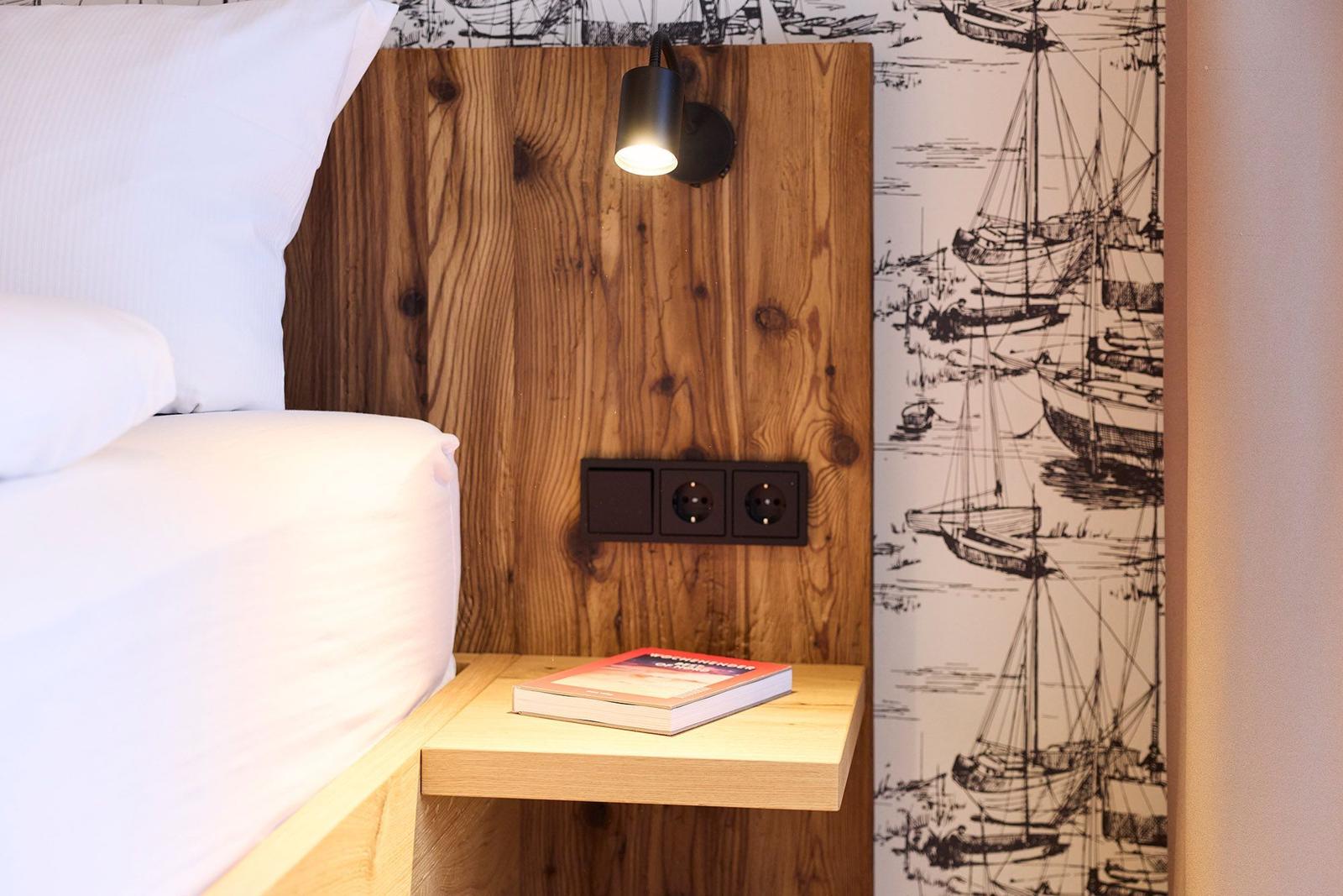 Schlafzimmer mit Holzkopfteil, Nachttisch und Segelyacht-Wandtapete.
