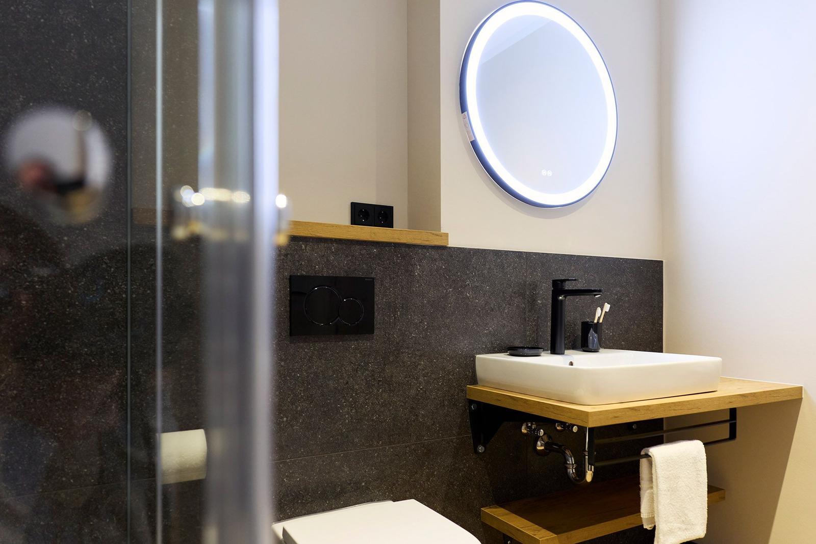 Badezimmer mit Dusche, Waschbecken und beleuchtetem Spiegel.