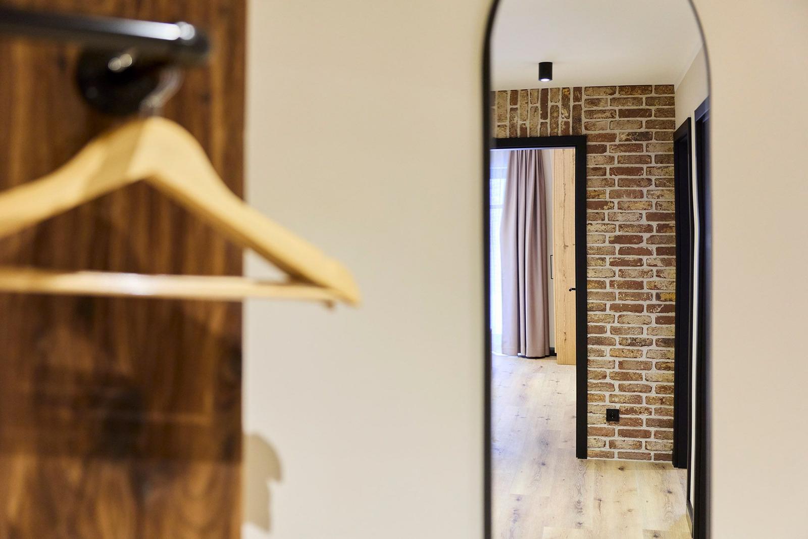 Spiegel zeigt Flur mit Backsteinwand und Holzboden. Kleiderhaken im Vordergrund.