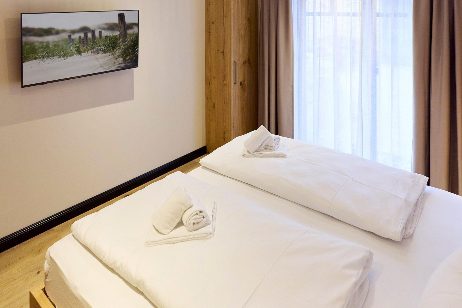 Zwei Betten mit weißen Bettwäsche, Holzschrank und Fenster mit Vorhängen.