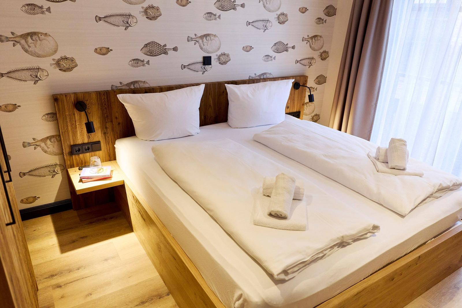 Schlafzimmer mit Holzbett, Fischmotiv-Wand und Fenster mit Vorhängen.