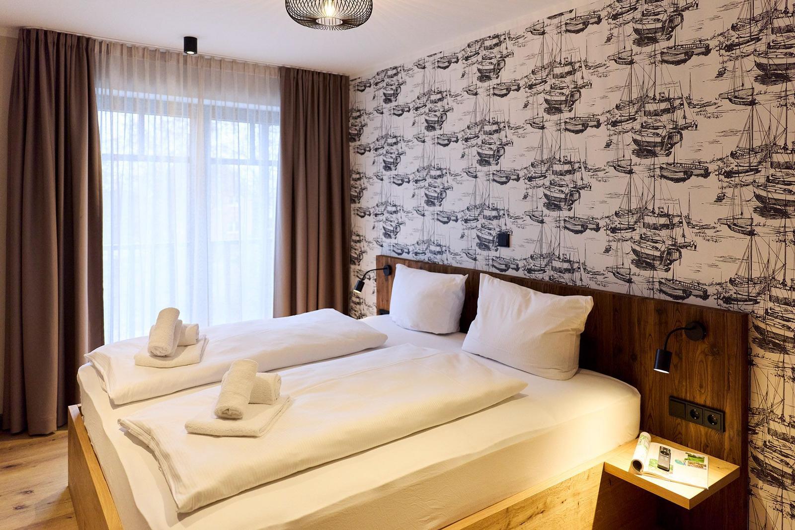 Schlafzimmer mit Bett, Vorhängen und Wandtapete mit Schiffsmotiven.