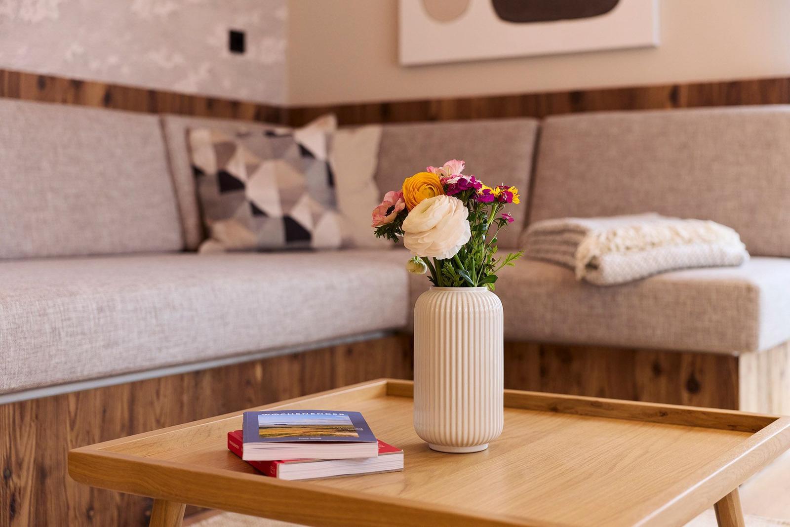 Ein Wohnzimmer mit Sofa, Tisch und Blumen in einem Vasen