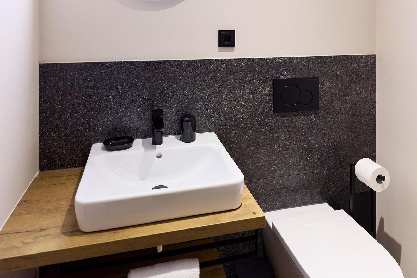 Badezimmer mit Waschbecken auf Holzplatte, schwarzer Wand und Toilette.