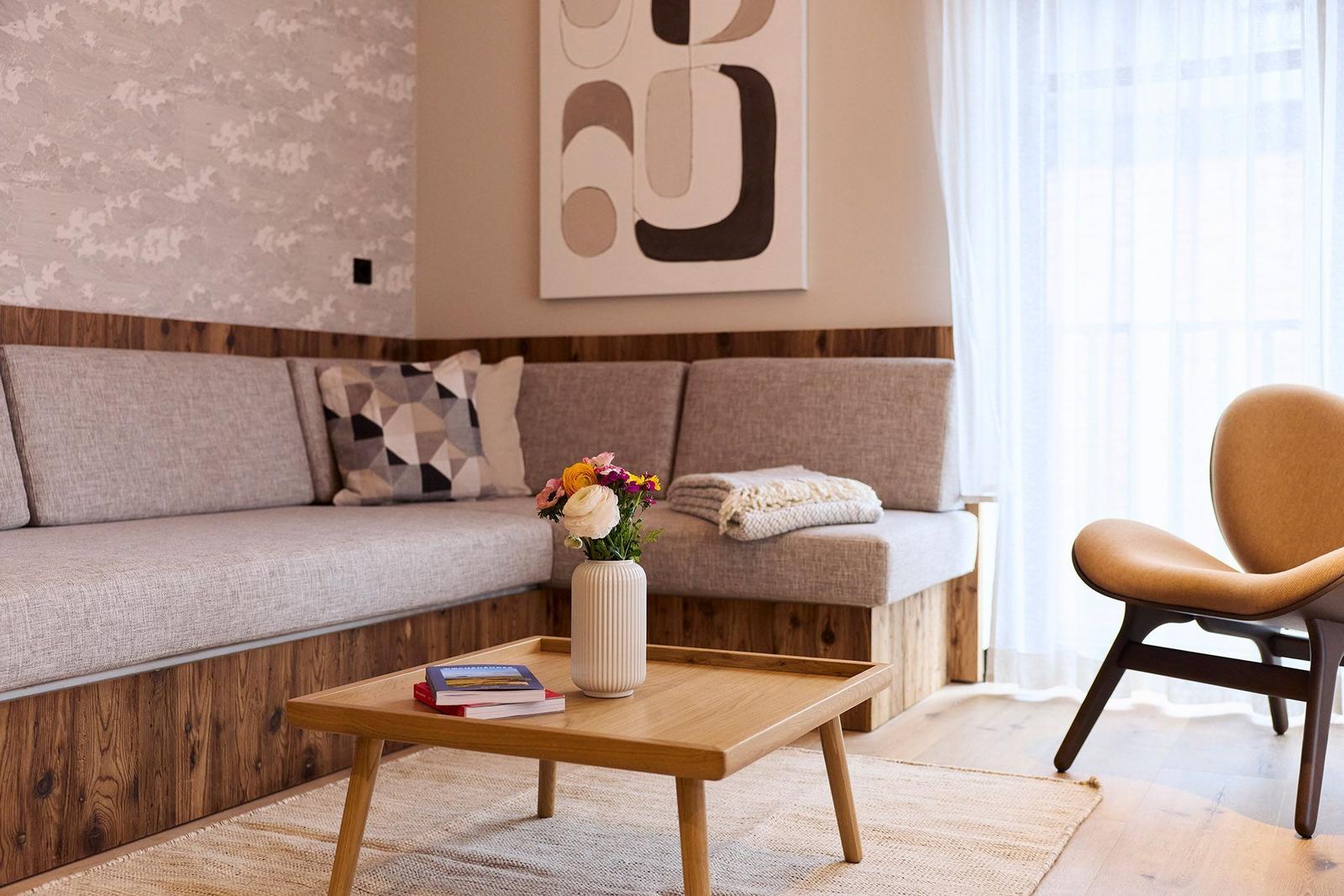Ein Wohnzimmer mit Sofa, Holztisch und Sessel. Auf dem Tisch steht eine Vase mit Blumen.