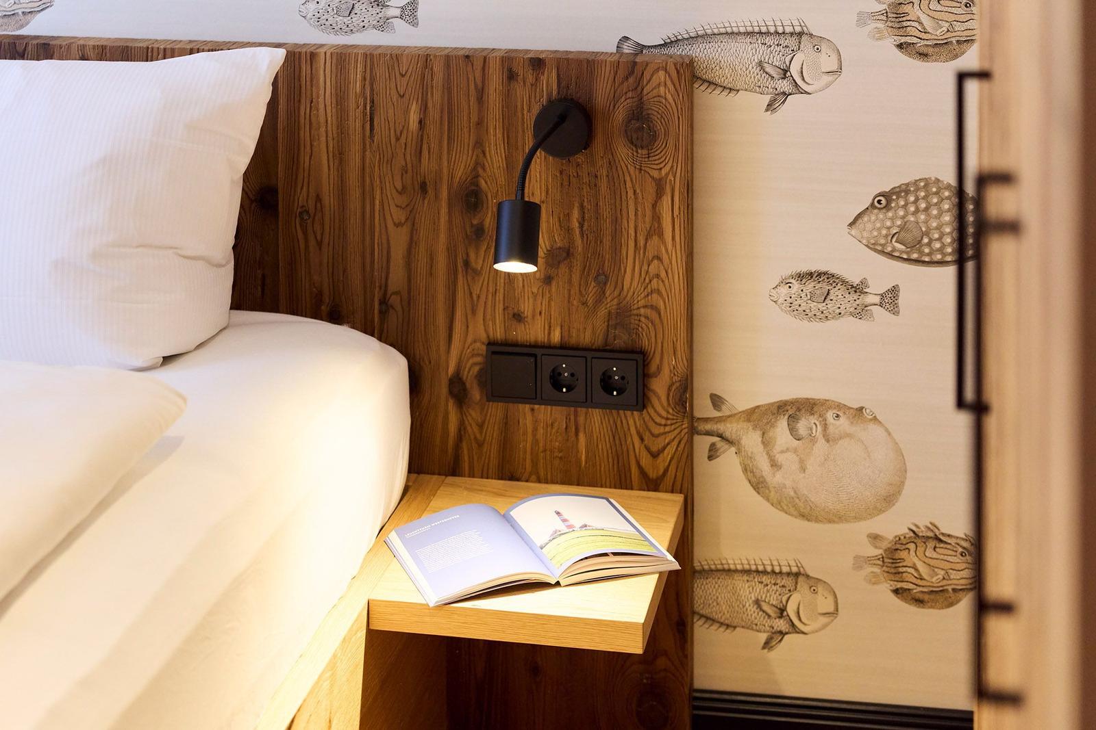 Bettkopfteil aus Holz, Wand mit Fischmotiven, Nachttisch mit Buch und Lampe.