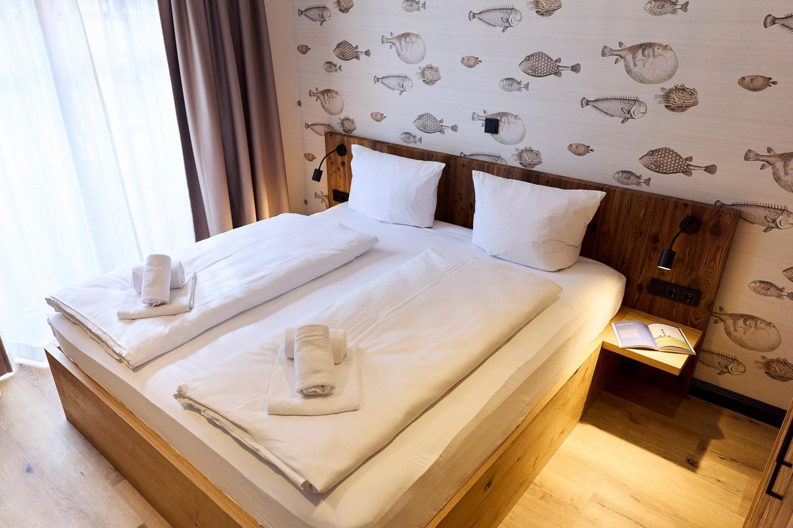 Doppelbett mit weißen Laken, Fischmotiv-Wand und Holzrahmen.