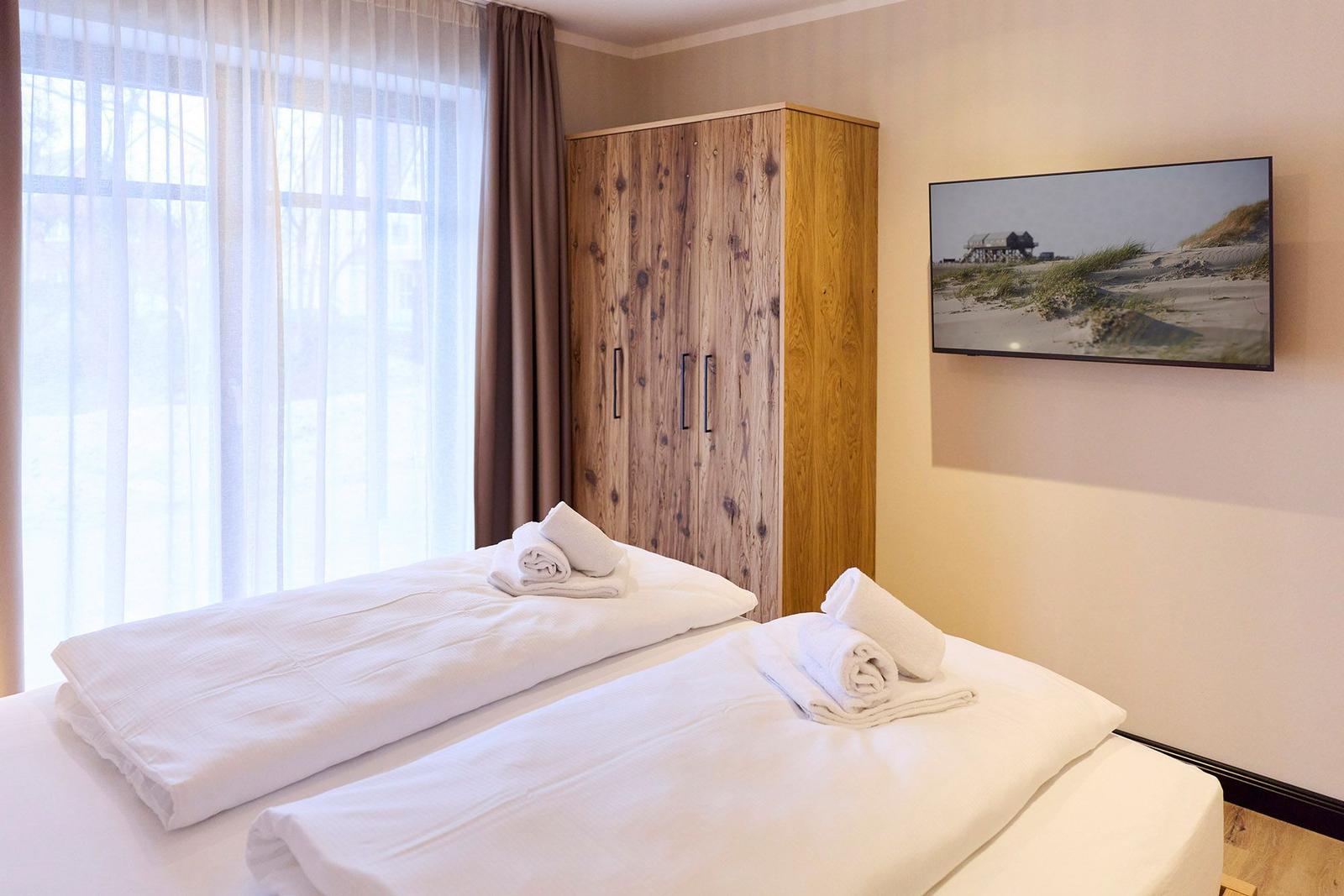 Zwei Betten mit weißen Bettwäsche, Holzschrank und Wandbild mit Strandmotiv.
