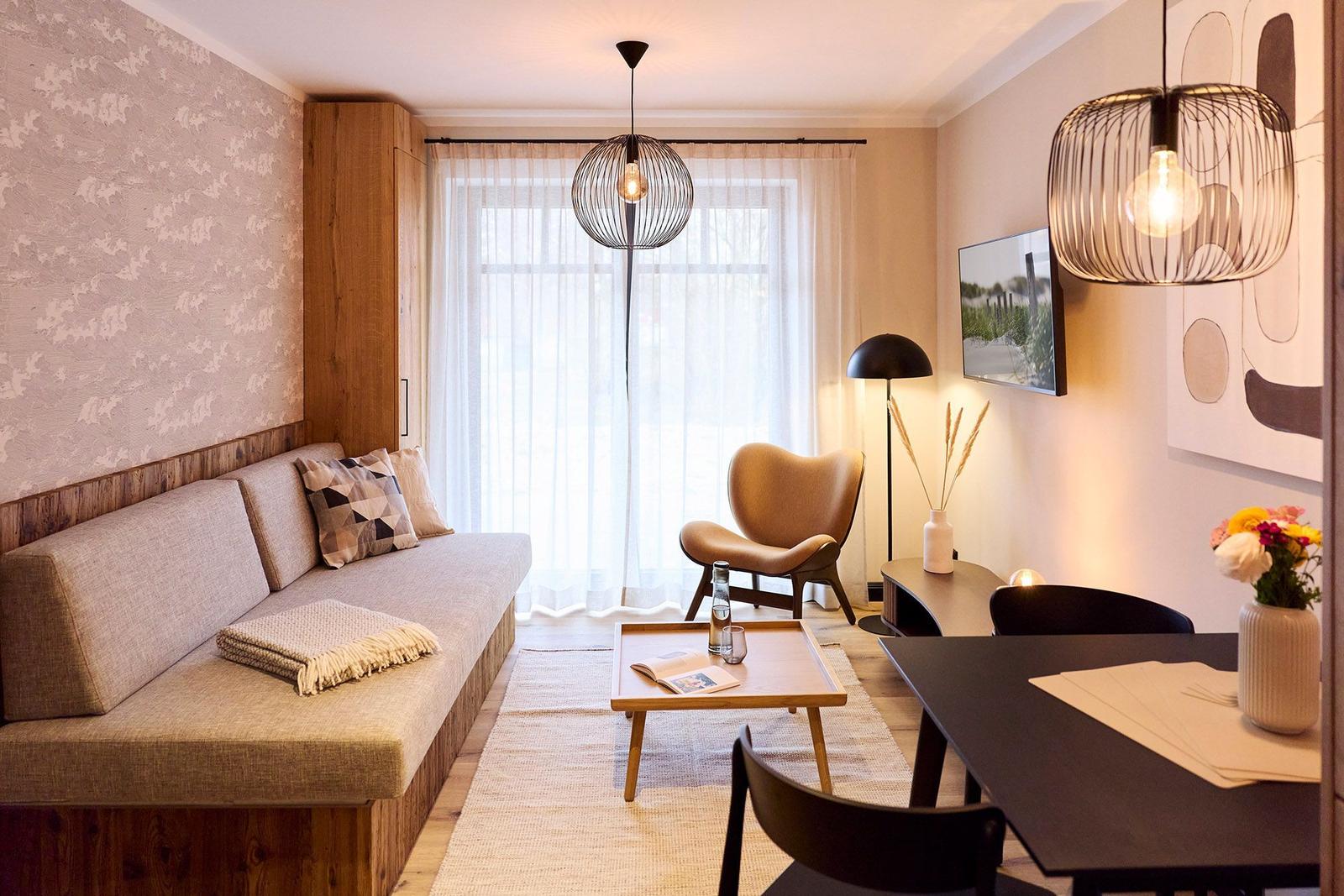 Wohnzimmer mit Sofa, Sessel, Tisch und Essbereich. Wand mit Tapete und Holzverkleidung.