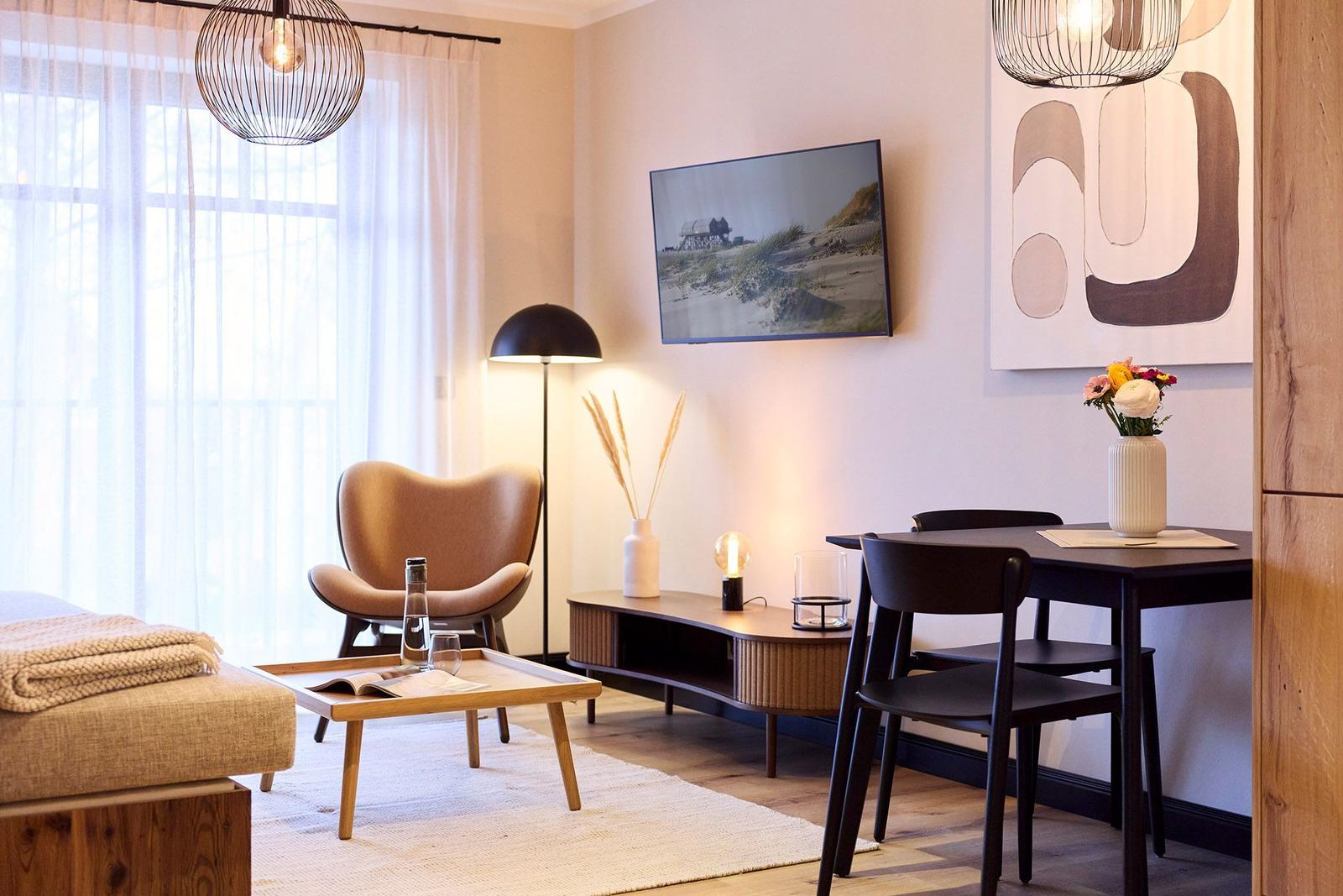 Wohn- und Essbereich mit Sofa, Stuhl, Tisch und Fernseher an der Wand.