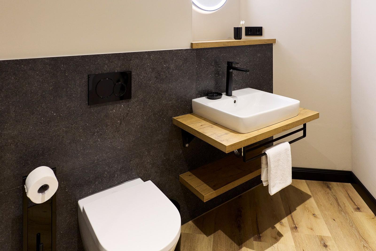 Badezimmer mit Toilette, Waschbecken auf Holzkonsole und runder Spiegel.