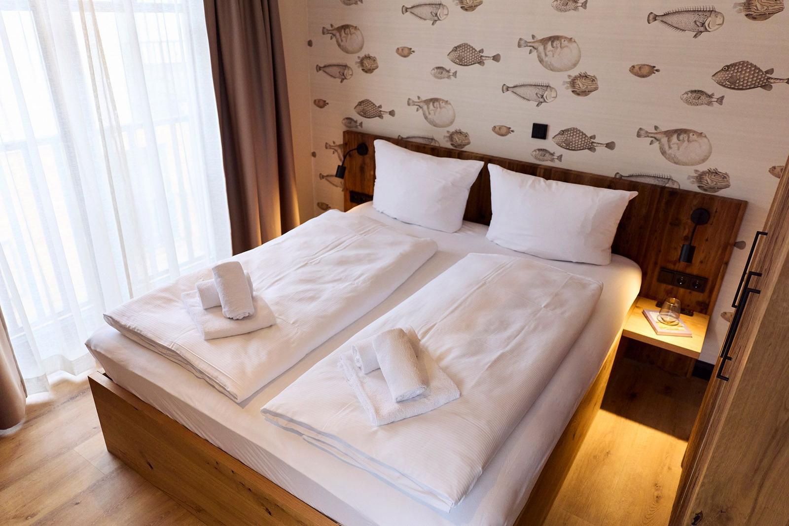 Doppelbett mit weißen Bettwäsche und Fischmotiv-Wandtapete.