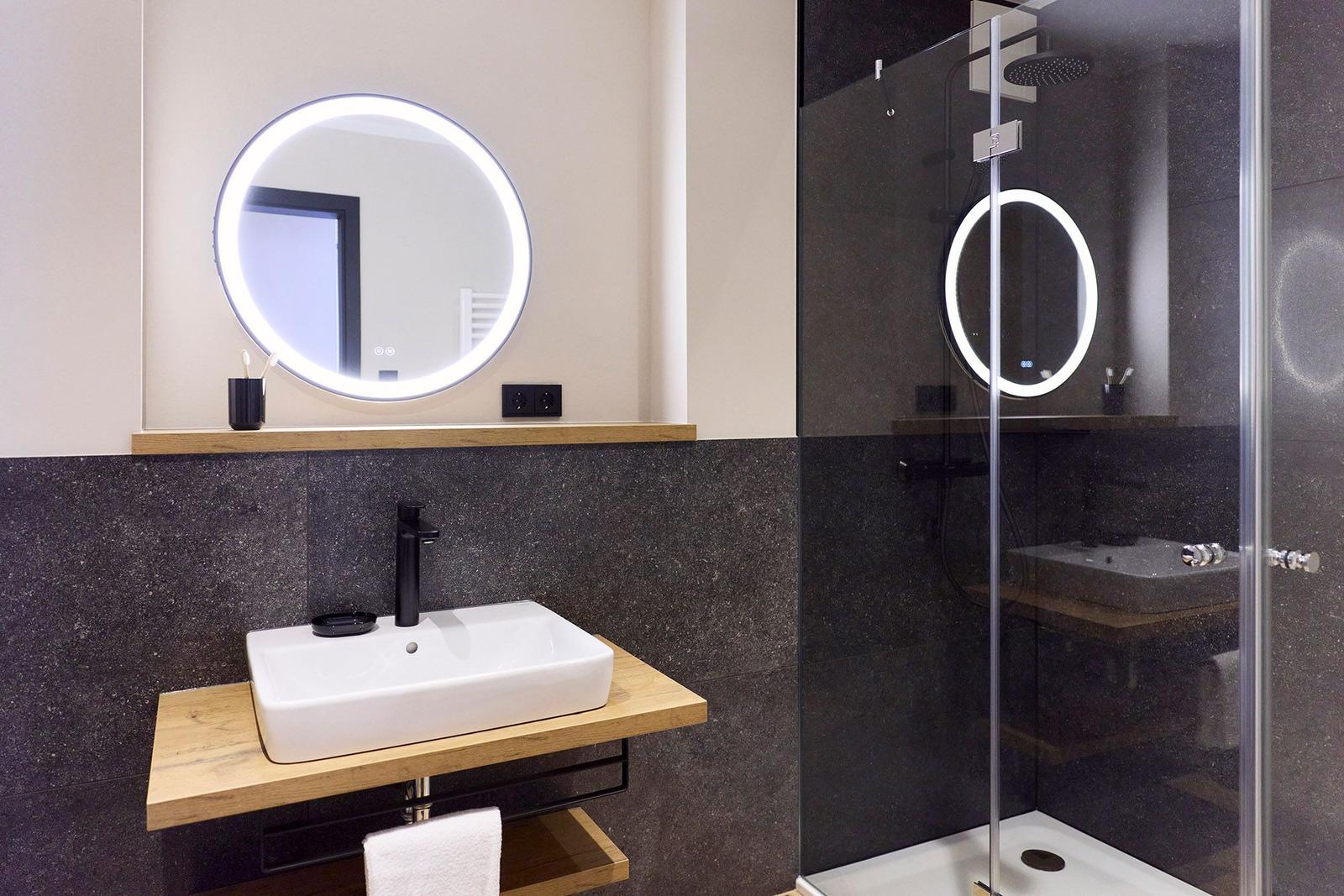 Badezimmer mit Dusche, Waschbecken und beleuchtetem Spiegel.