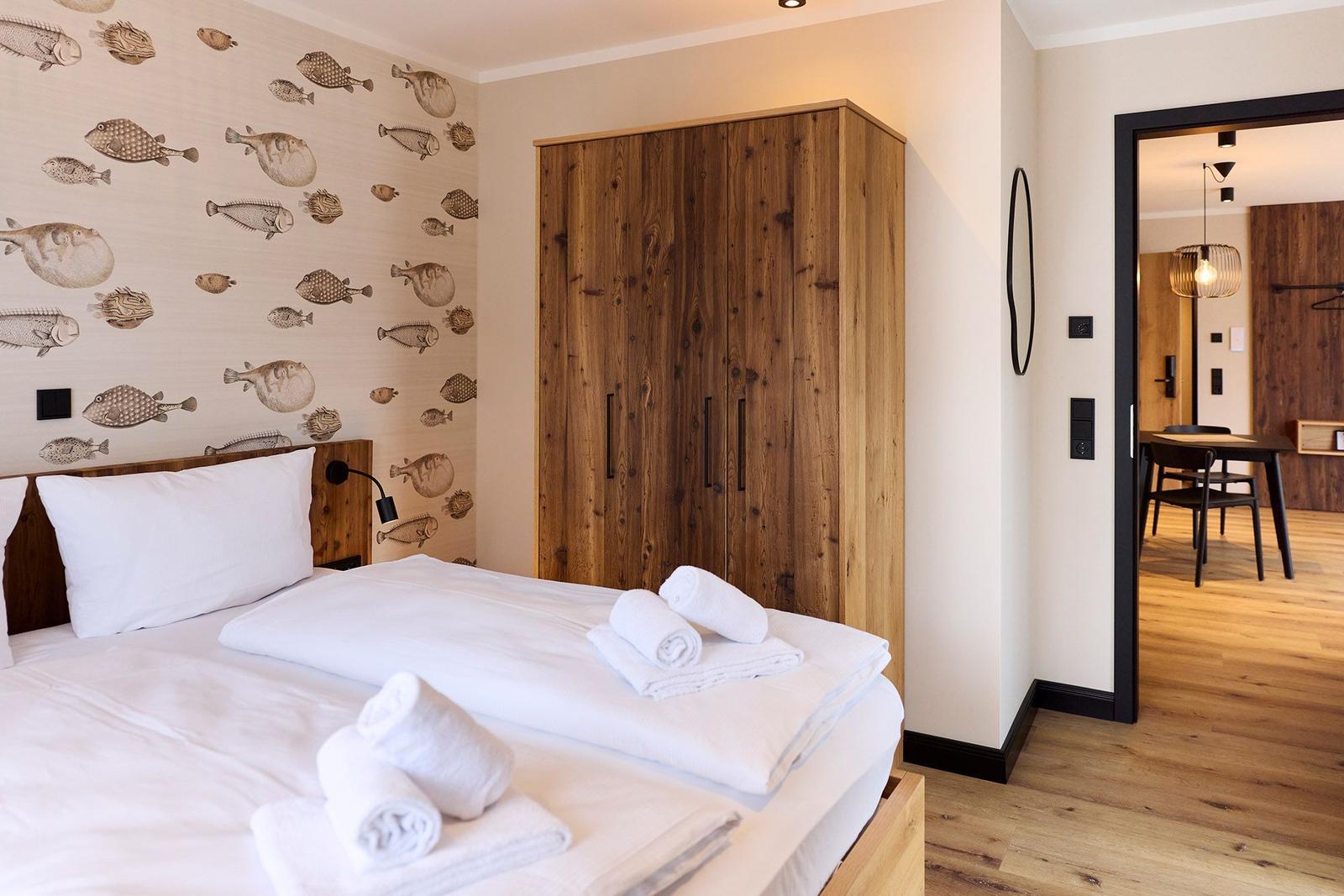 Schlafzimmer mit Bett, Holzschrank und Fischmotiv-Wandtapete. Durchgang zur Küche.