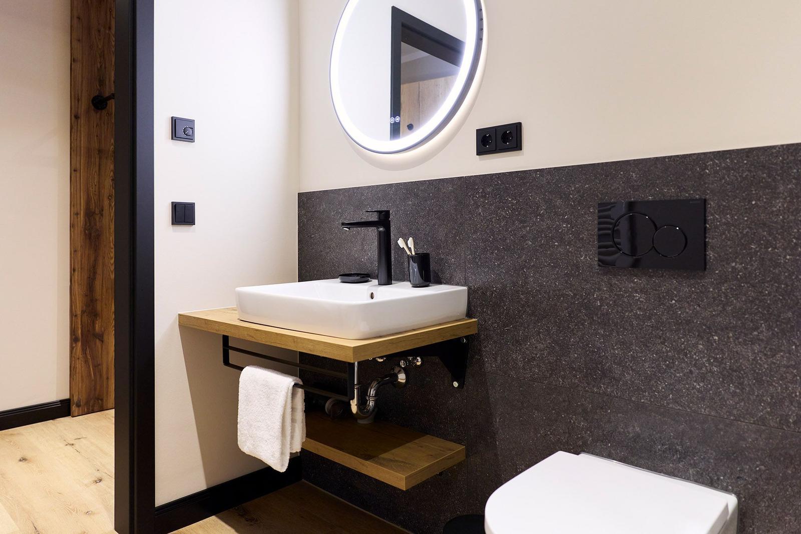 Badezimmer mit Waschbecken auf Holzkonsole, beleuchtetem Spiegel und Toilette.