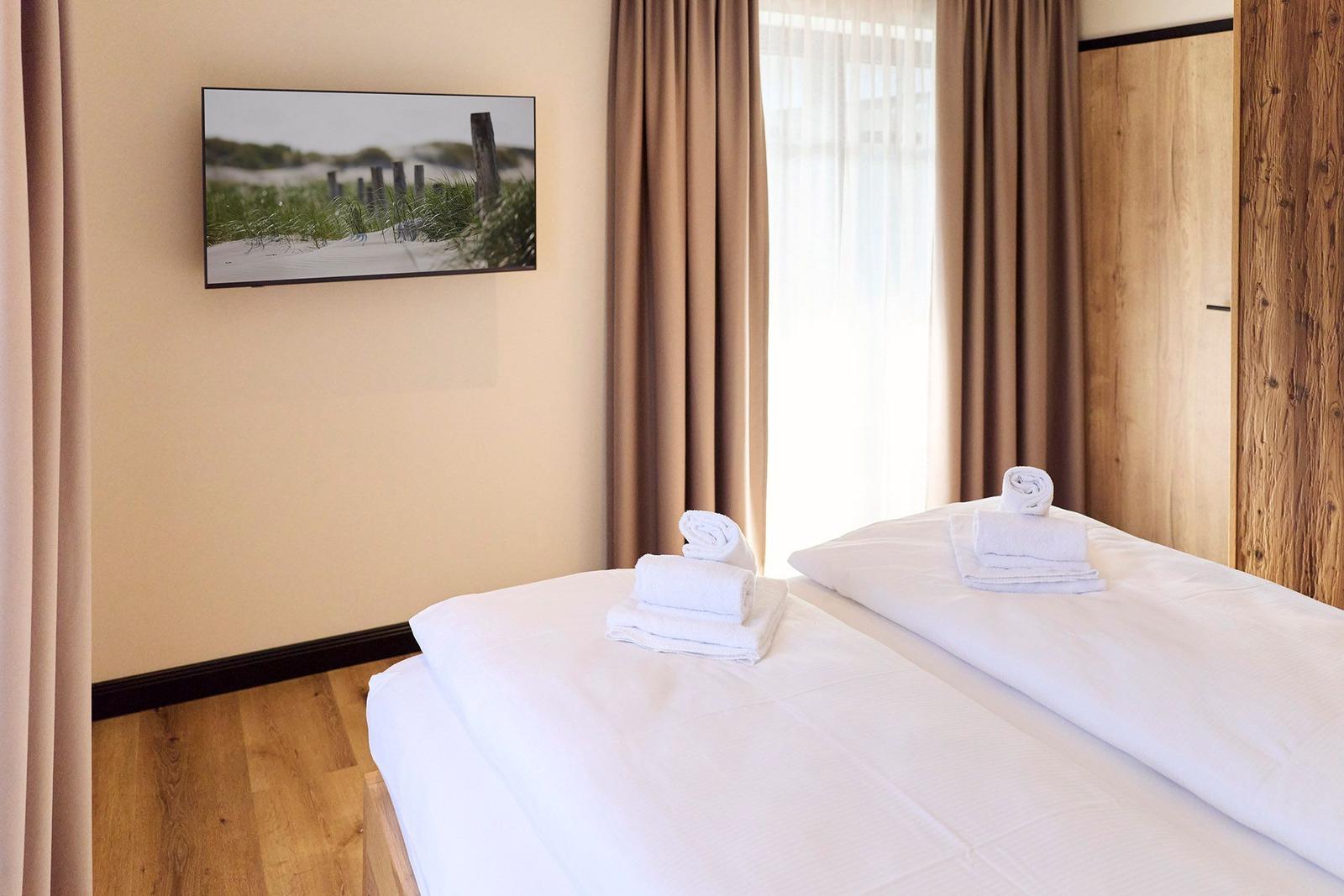 Zimmer mit Bett, weißen Bettwäsche, Handtüchern und Fenster mit Vorhängen.