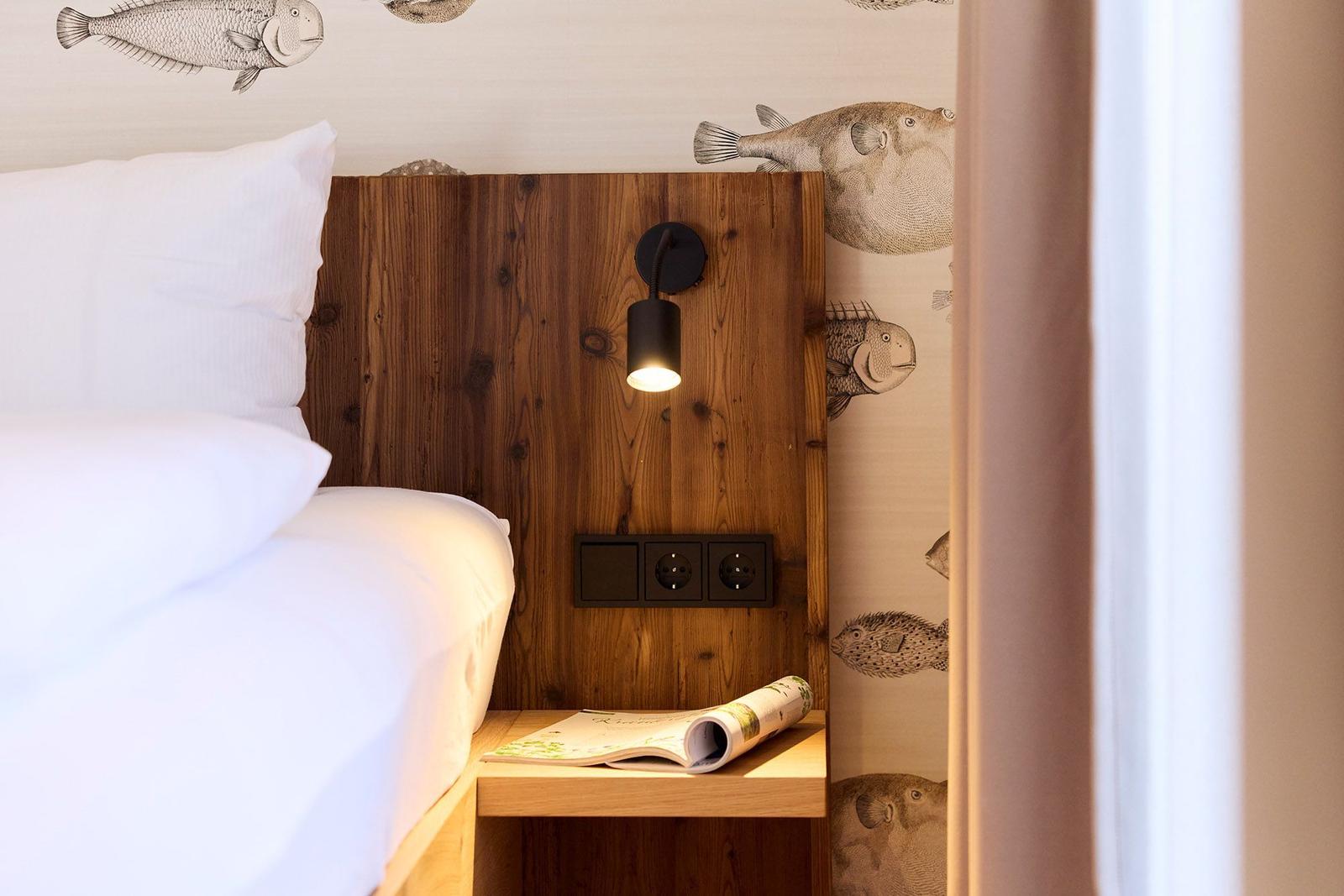Schlafzimmer mit Holz-Kopfteil, Fisch-Wandtapete und Nachttisch mit Zeitschrift.