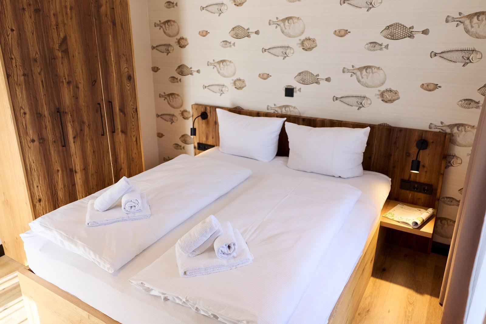 Doppelbett mit weißen Laken, Fischmotiv-Wand und Holzmöbel.