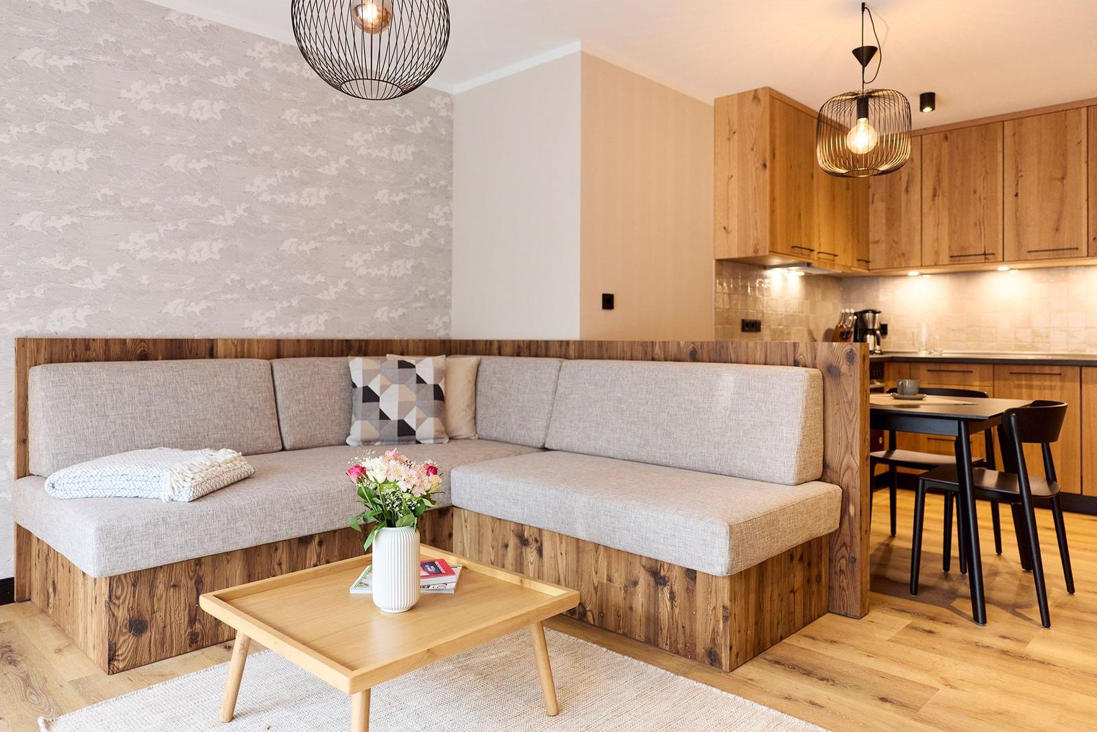 Wohnbereich mit Sitzbank, Couchtisch und Küchenbereich im Hintergrund.