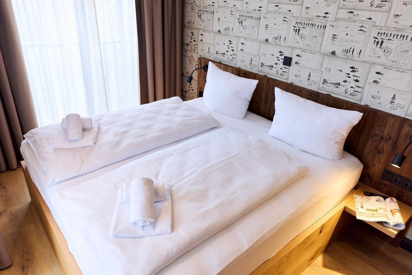 Ein Bett mit weißer Bettwäsche, Handtüchern und einem Holzgestell. An der Wand hängt eine gestaltete Tapete.