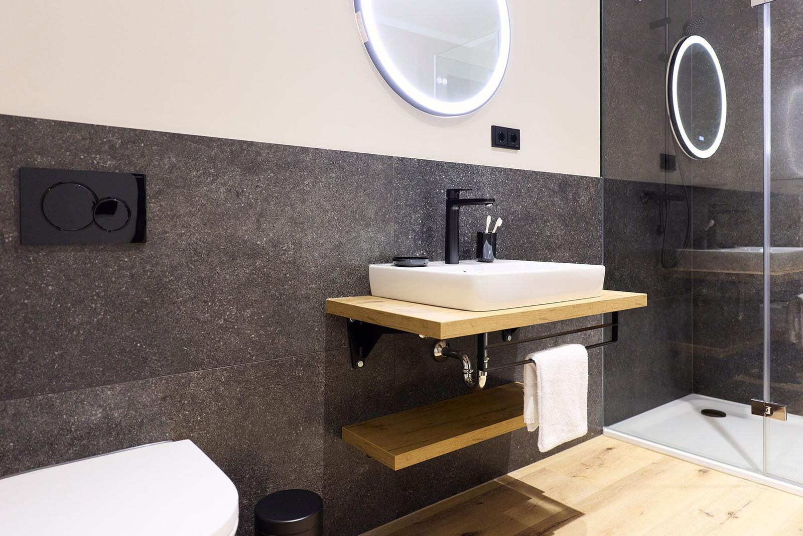 Badezimmer mit Waschbecken auf Holzkonsole, runden Spiegel und Dusche mit Glaswand.