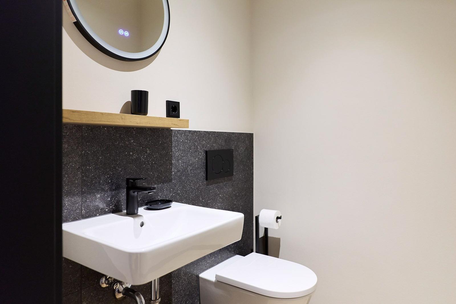 Badezimmer mit Waschbecken, Toilette und runden Spiegel.