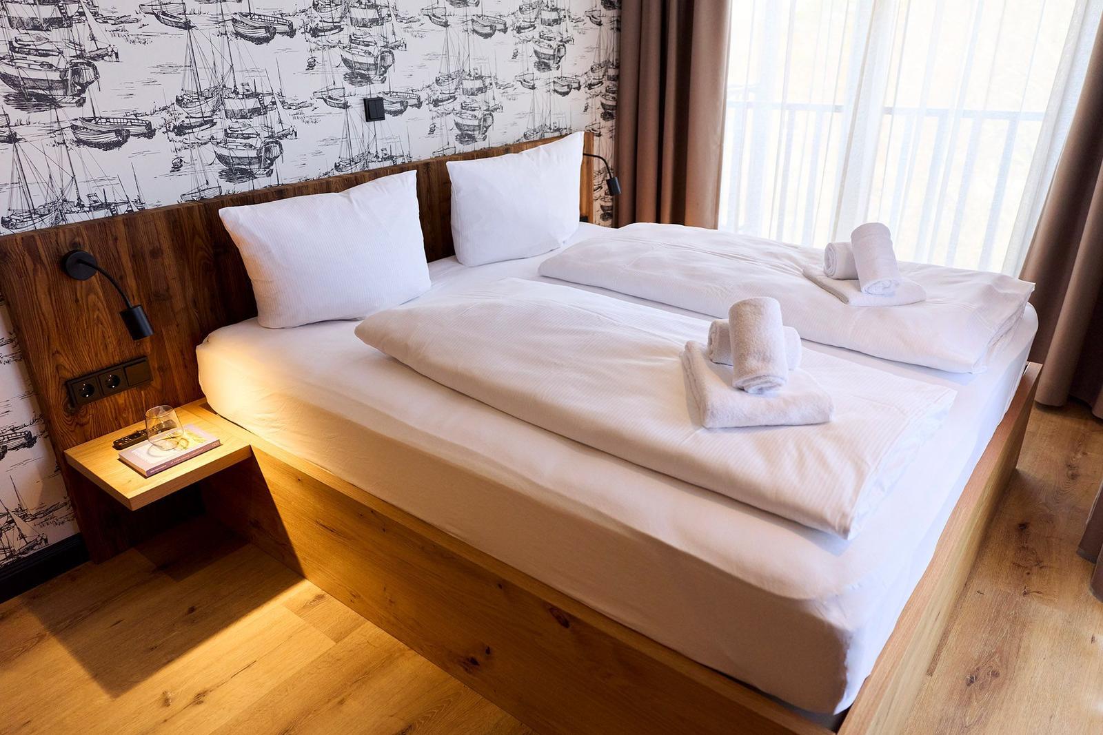 Ein Bett mit weißen Laken und Handtüchern. Wand mit Segelyacht-Motiv und Holzrahmen.