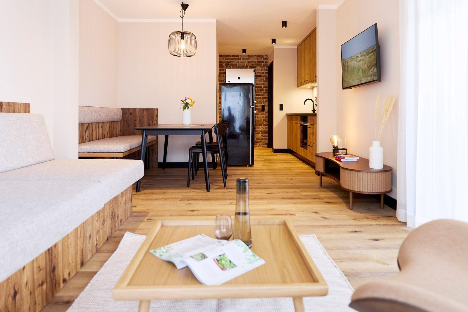 Wohn- und Essbereich mit Holzboden, Esstisch, Sofa und Küchenbereich im Hintergrund.