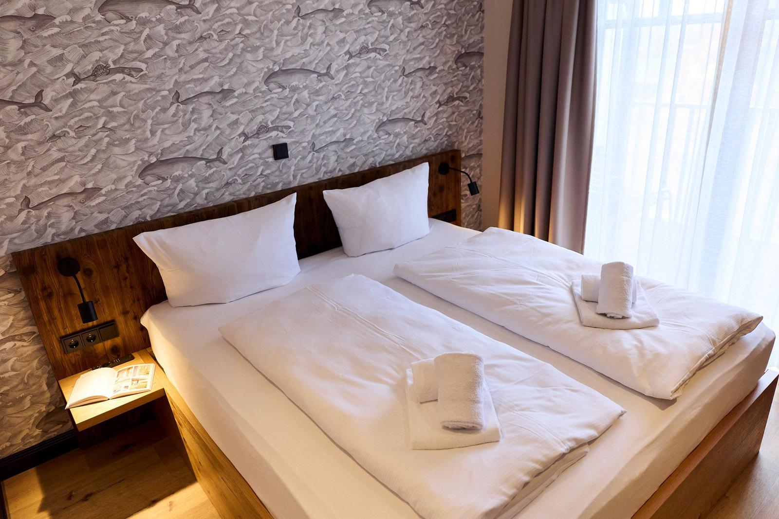 Doppelbett mit weißen Bettwäsche und Handtüchern. Wandtapete mit Walenmotiv und Holzgestell.