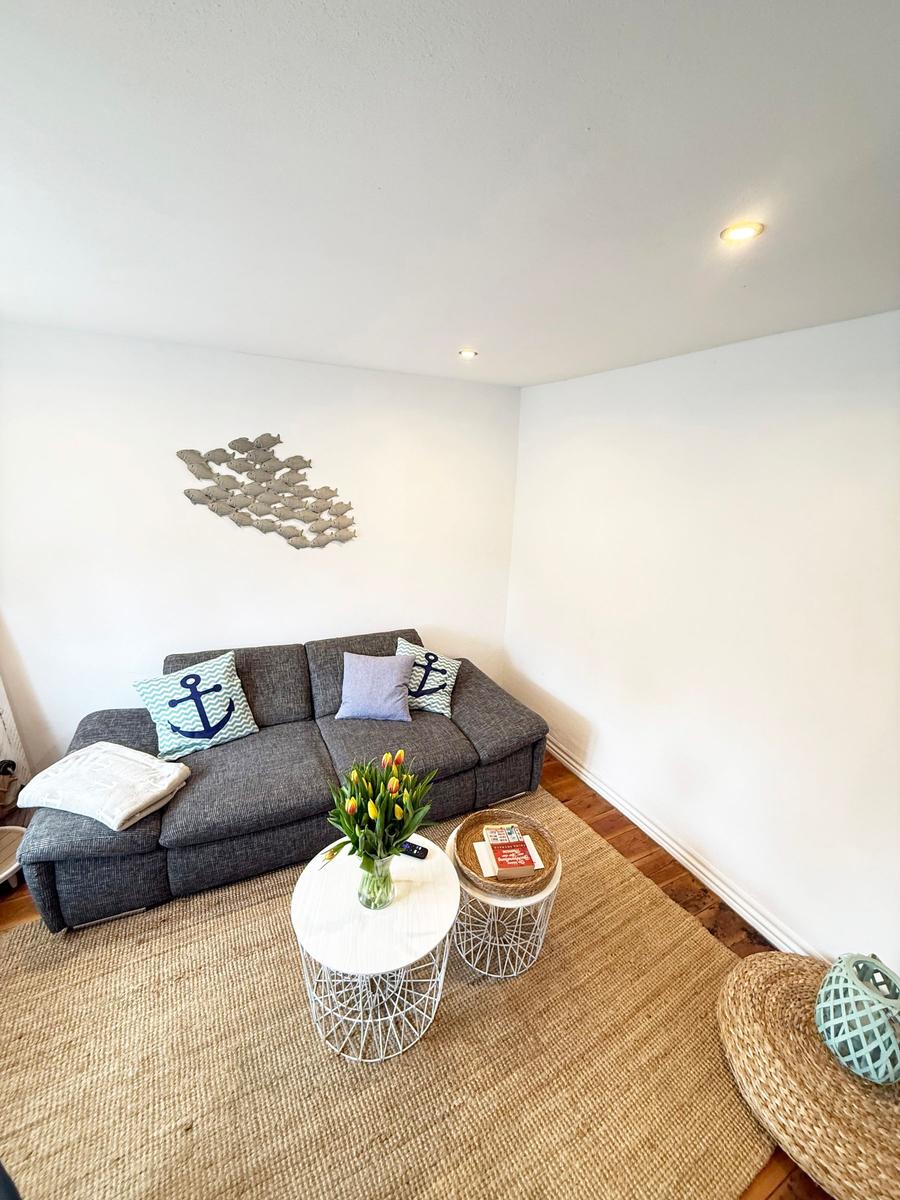Ein Wohnzimmer mit grauem Sofa, zwei runden Tischen und einem Wandbild aus Fischen.