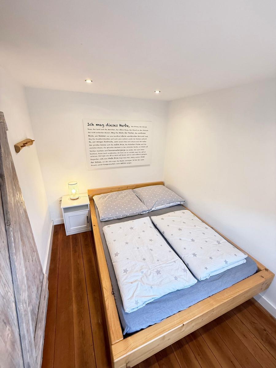 Schlafzimmer mit Holzbett, Nachttisch und Wandbild. Holzfußboden und weiße Wände.