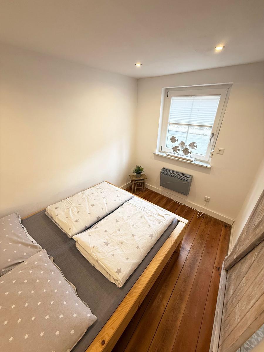 Schlafzimmer mit Holzboden, Bett und Fenster mit Jalousie.