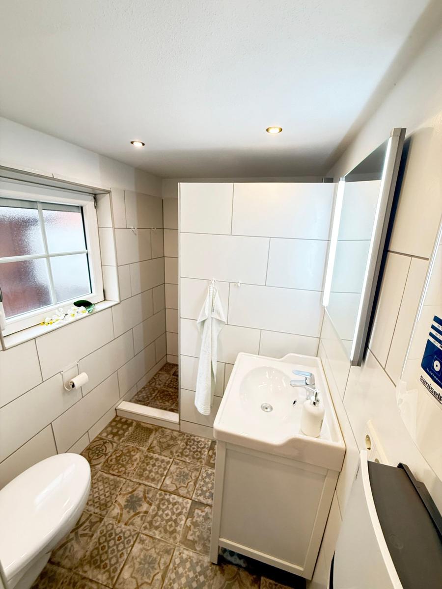 Badezimmer mit Waschbecken, Toilette und Dusche. Fliesenboden und Spiegelschrank.
