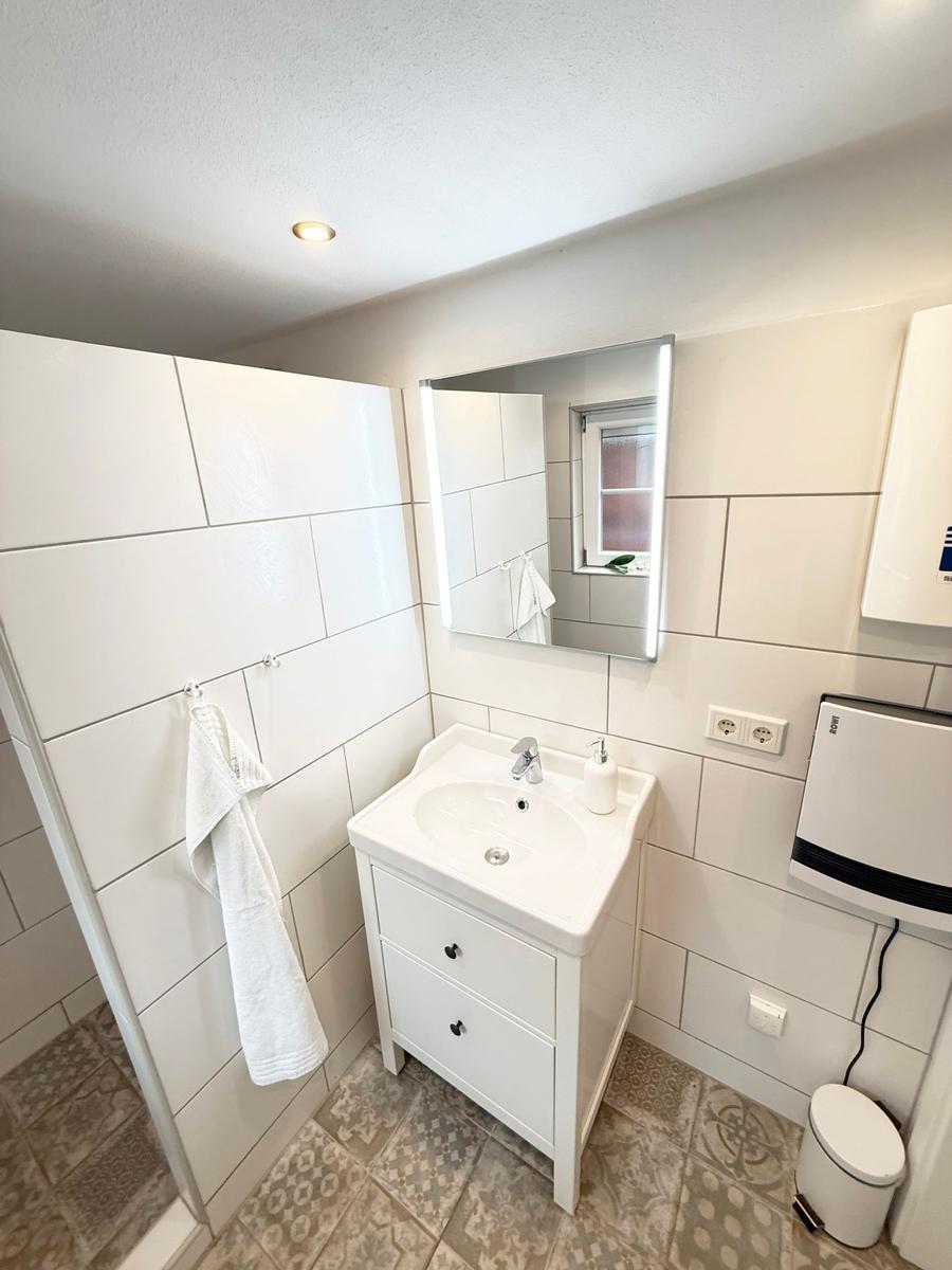 Badezimmer mit Waschbecken, Spiegel, Dusche und Toilette.