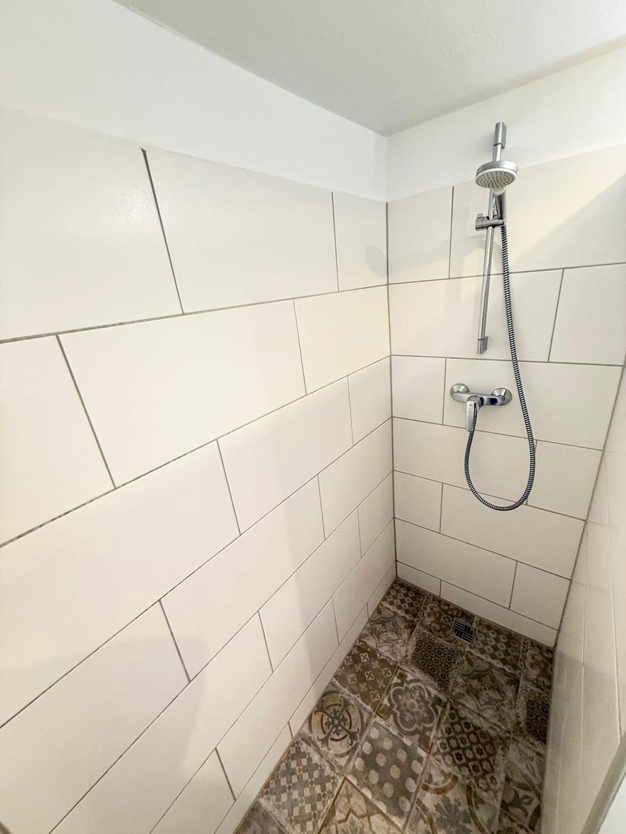 Dusche mit weißen Wänden und gemustertem Boden