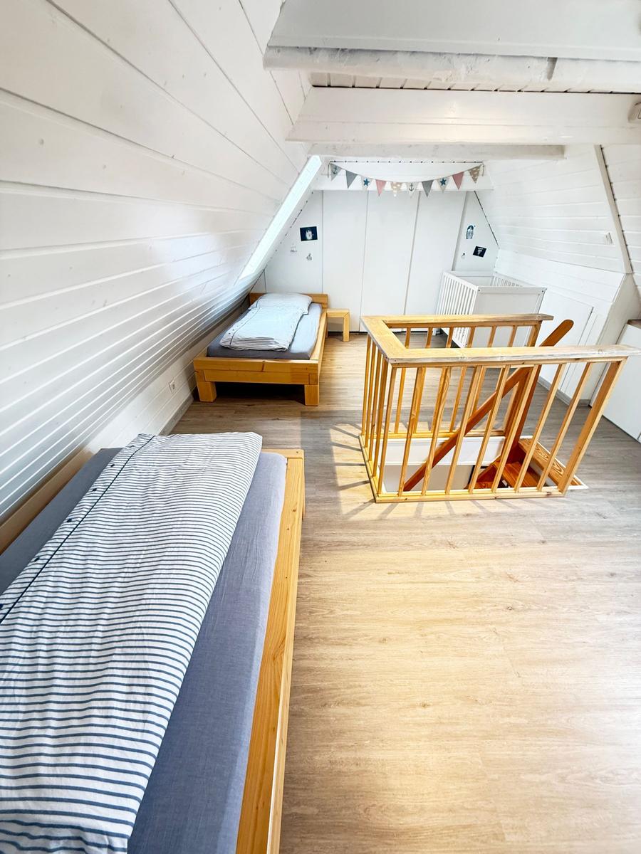 Zimmer mit zwei Betten, Holzgeländer und Dachschrägen. Weiße Wände und Holzboden.