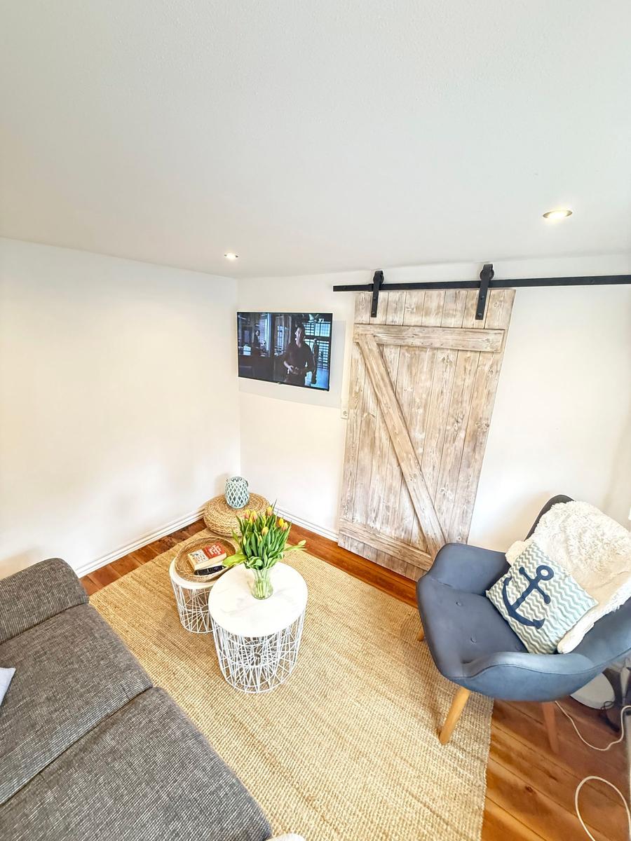 Wohnzimmer mit Sofa, Sessel, Fernseher und Schiebetür
